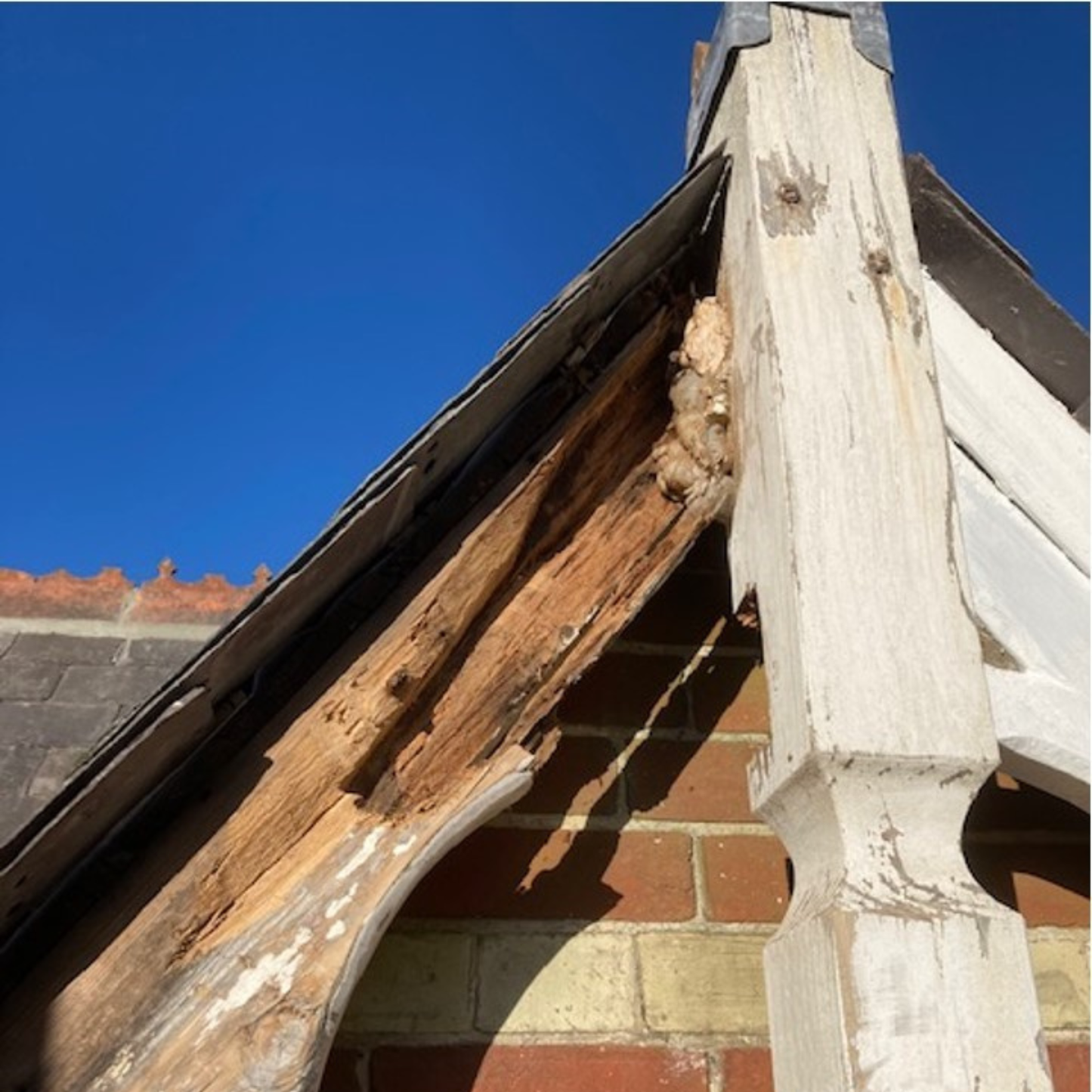 Damaged wooden roof structure with blue sky in the background. Rotten gable end.