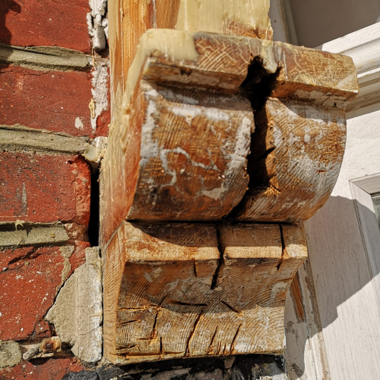 Close-up of a rotten wooden architectural detail on a building with a red brick wall.