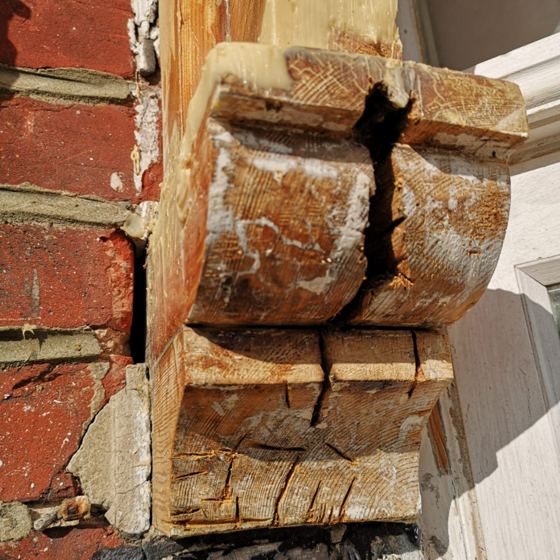 Close-up of a rotten wooden architectural detail on a building with a red brick wall.